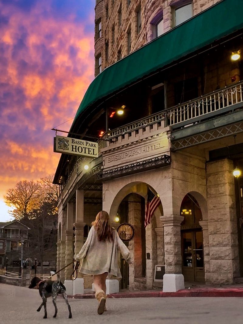 A traveler walking a dog past a historic stone hotel under a pink evening sky