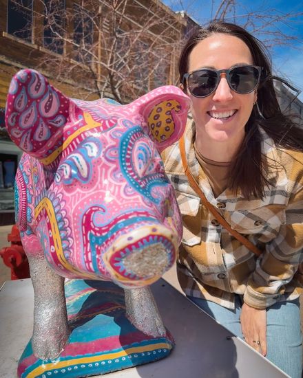 A creator in sunglasses taking a selfie beside a painted pig statue
