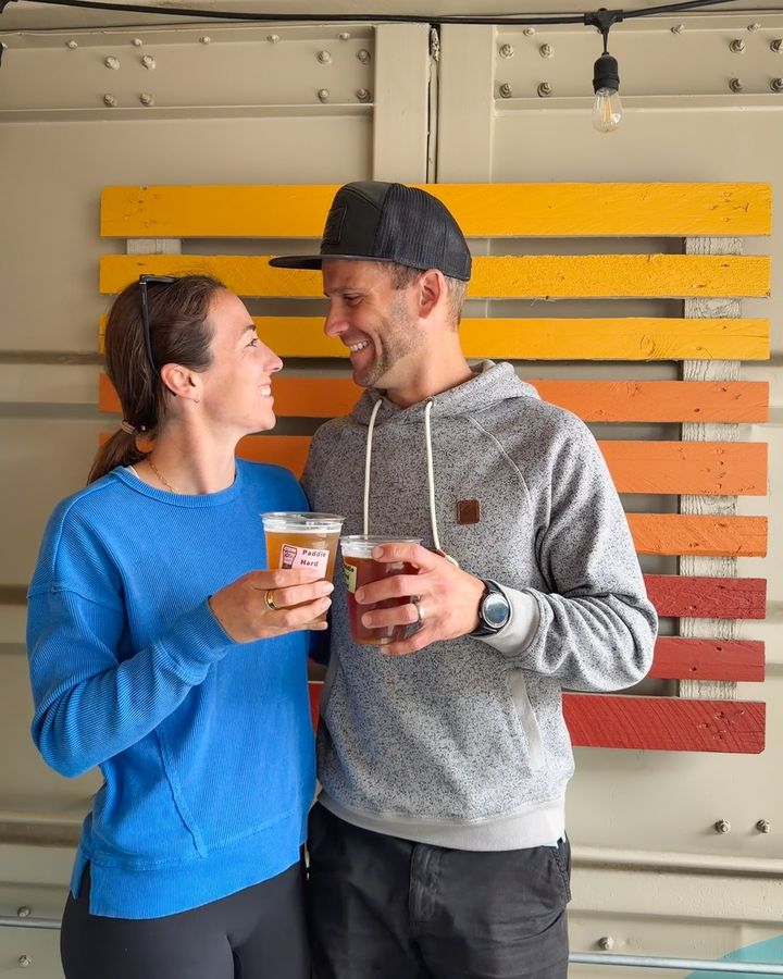 A smiling couple toasting with iced coffees in front of a colorful wall