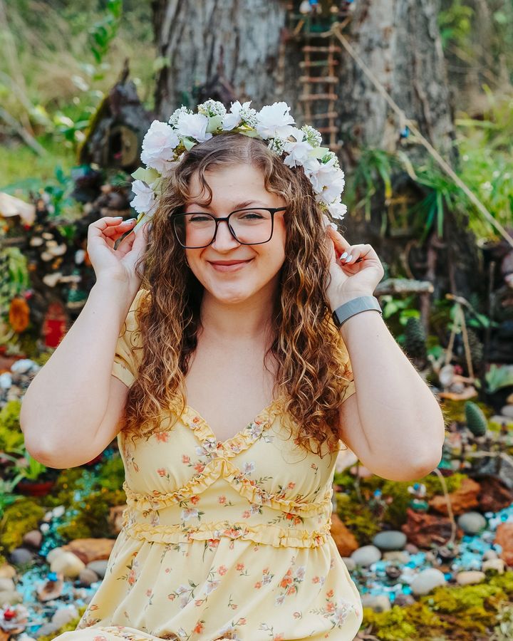 A smiling creator in a flower crown and sundress posing in a garden