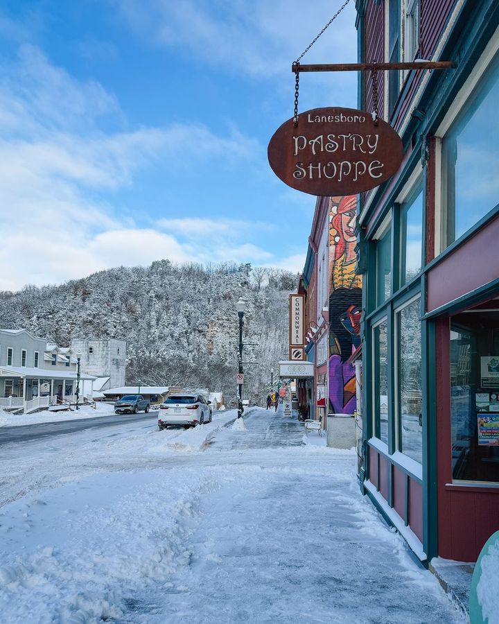 A snowy small-town main street with a hanging pastry shop sign