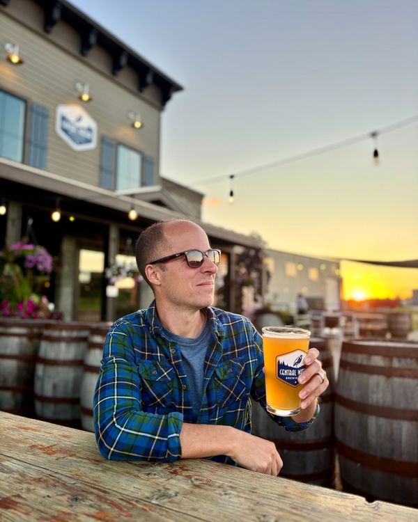 A man raising a pint of beer on a brewery patio at sunset