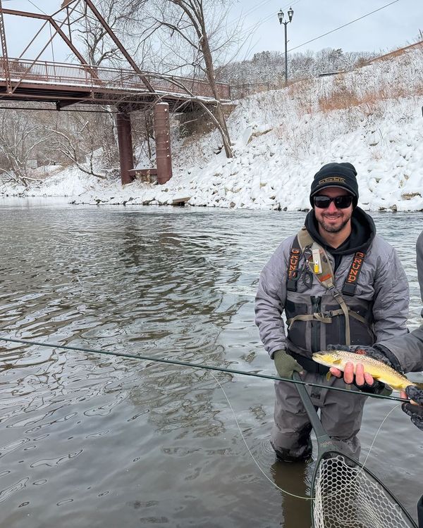 An angler standing in a winter river, holding up a freshly caught trout