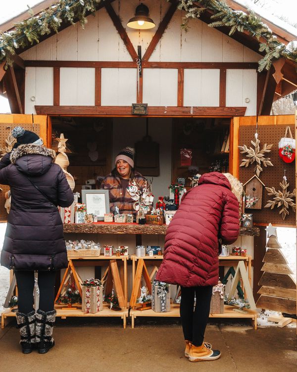 Shoppers browsing a wooden holiday market stall trimmed with garland